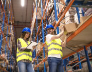Two young people working together in warehouse storage facility. Checking goods at distribution warehouse.